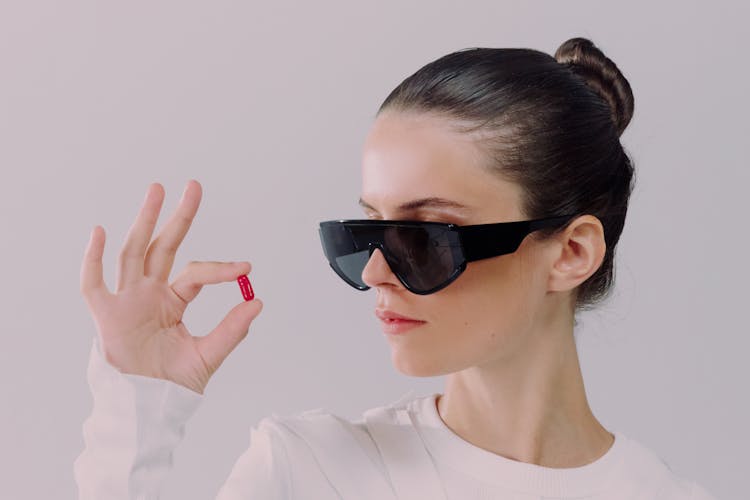 Studio Shot Of Woman In Sunglasses Holding Red Pill