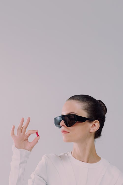 Studio shot of woman in sunglasses holding red pill