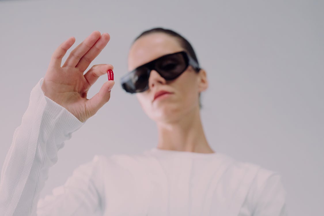 Studio shot of woman in sunglasses holding red pill · Free Stock Photo