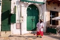 Woman sweeping outside an arched green door on a sunny day.