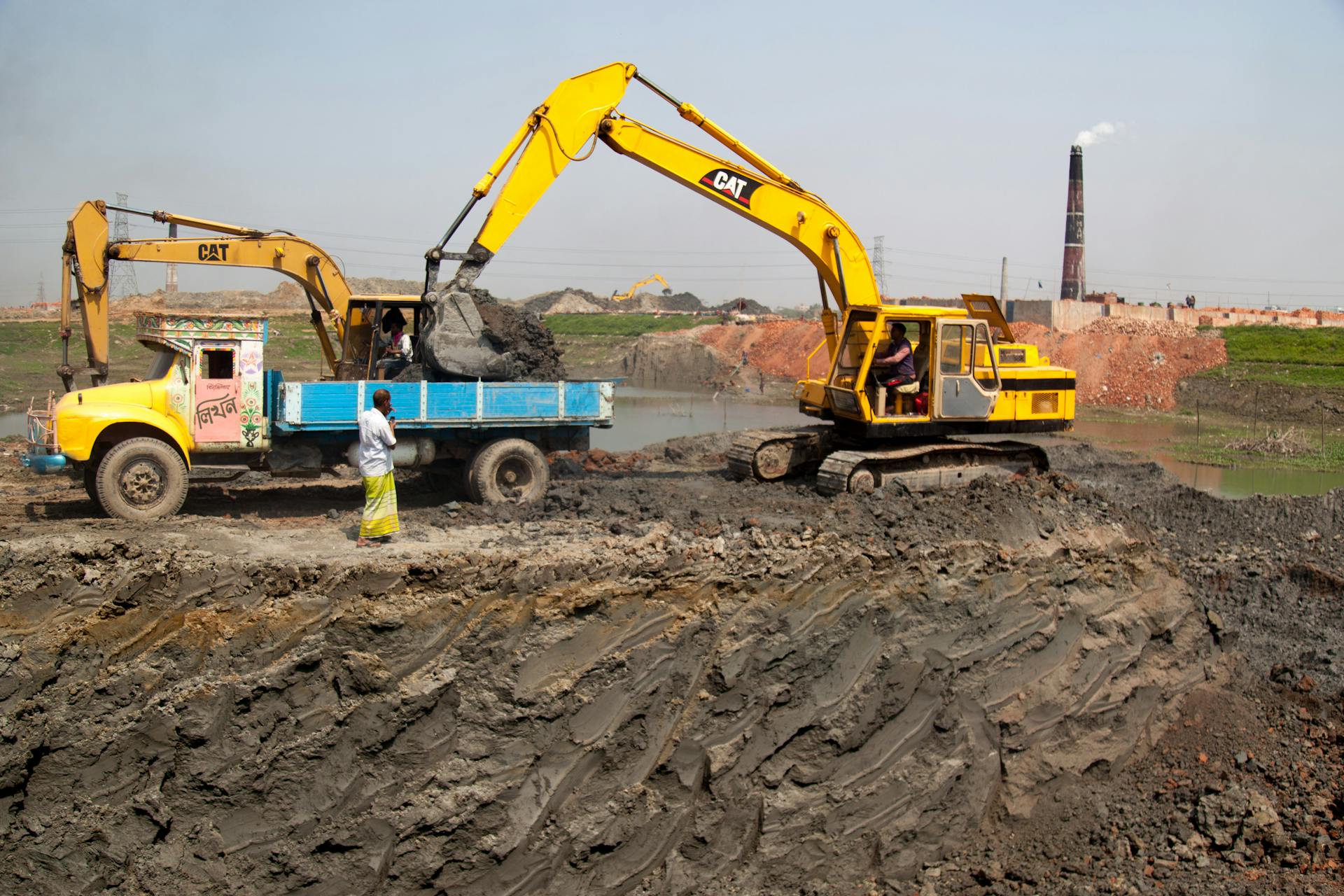 Excavators loading soil into trucks at a construction site in Dhaka, Bangladesh.