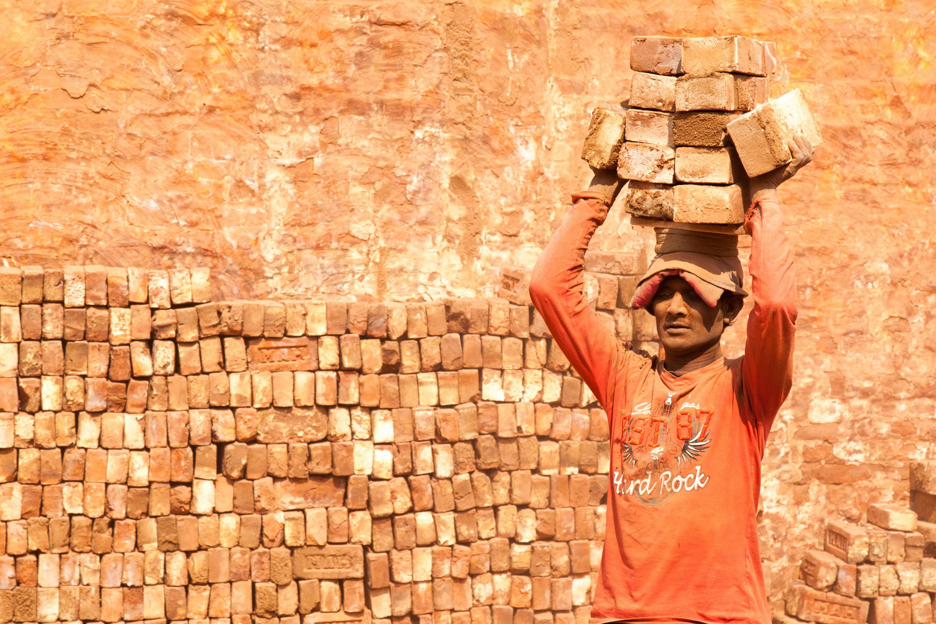 mann in red shirt carrying brick on his head