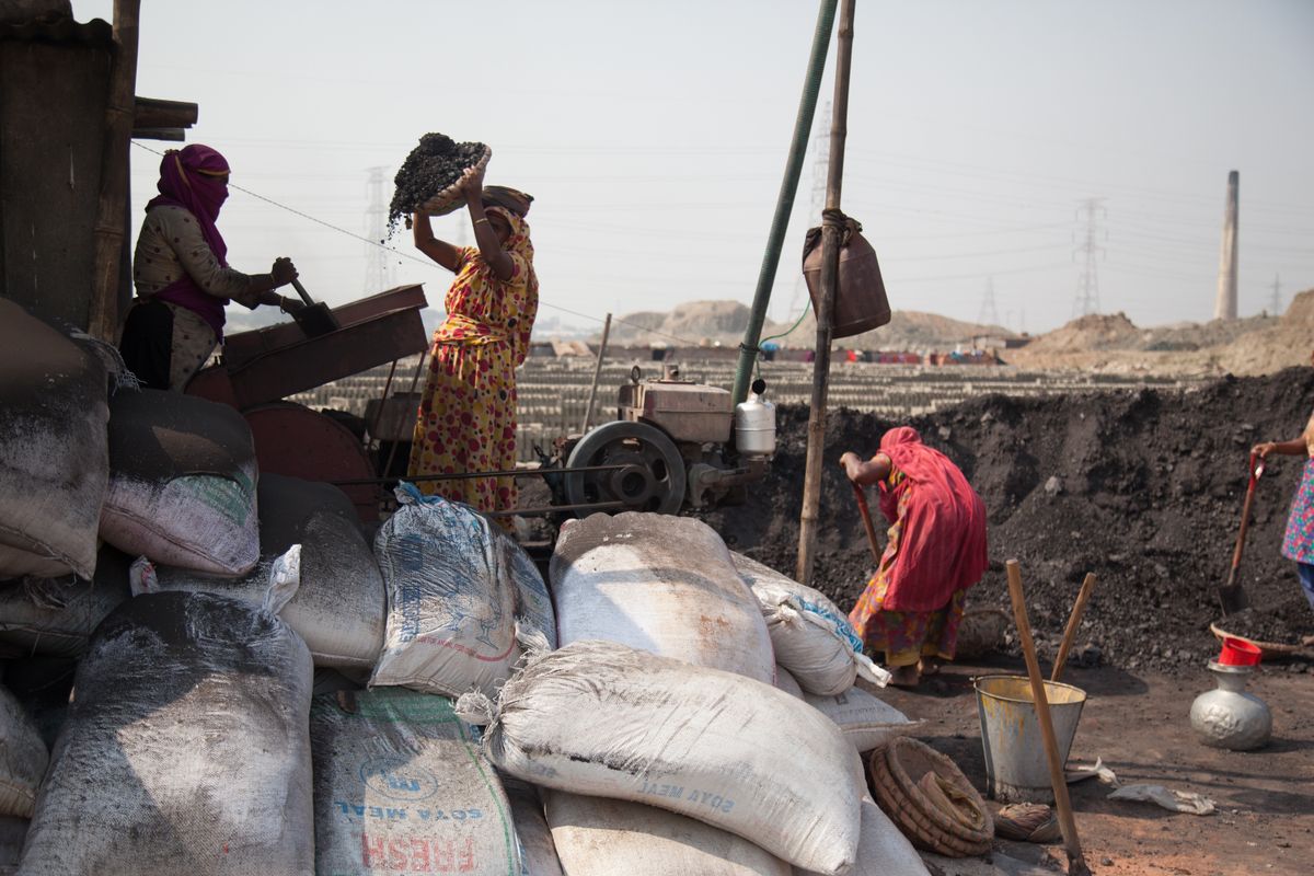 Women workers shoveling coal and clay at an outdoor brick kiln in South Asia