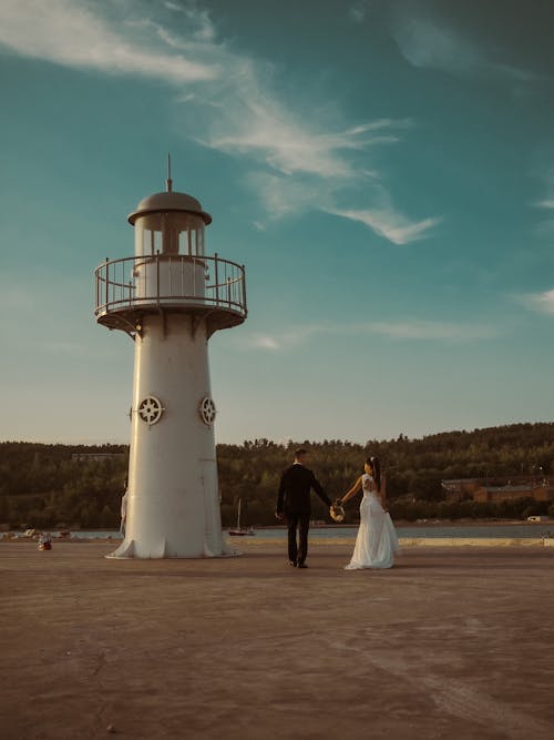 Free Bride and Groom Walking Beside a Lighthouse Stock Photo