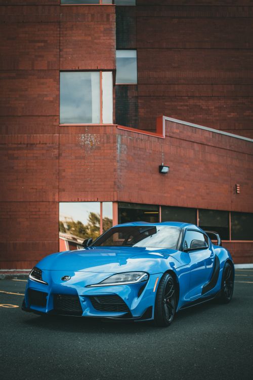 Free A shiny blue Toyota Supra parked in front of a brick building, showcasing its sleek design. Stock Photo
