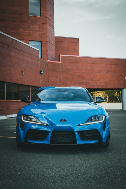 Free Front view of a sleek blue sports car parked in an urban setting with red brick architecture. Stock Photo