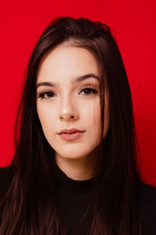 Free Beautiful portrait of a woman with long hair against a bold red background, showcasing elegance. Stock Photo