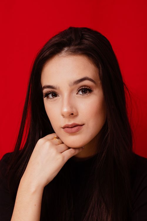 Free Sophisticated portrait of a young woman posing against a vibrant red backdrop. Stock Photo