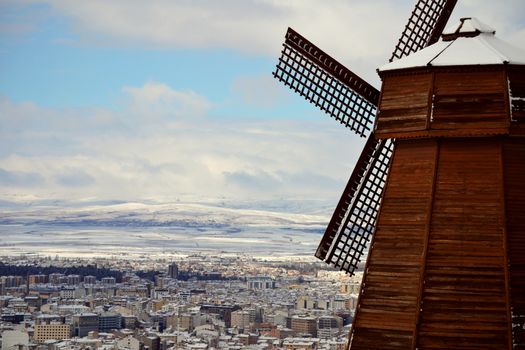 A picturesque view of a snow-covered city with a wooden windmill, set against a winter landscape.