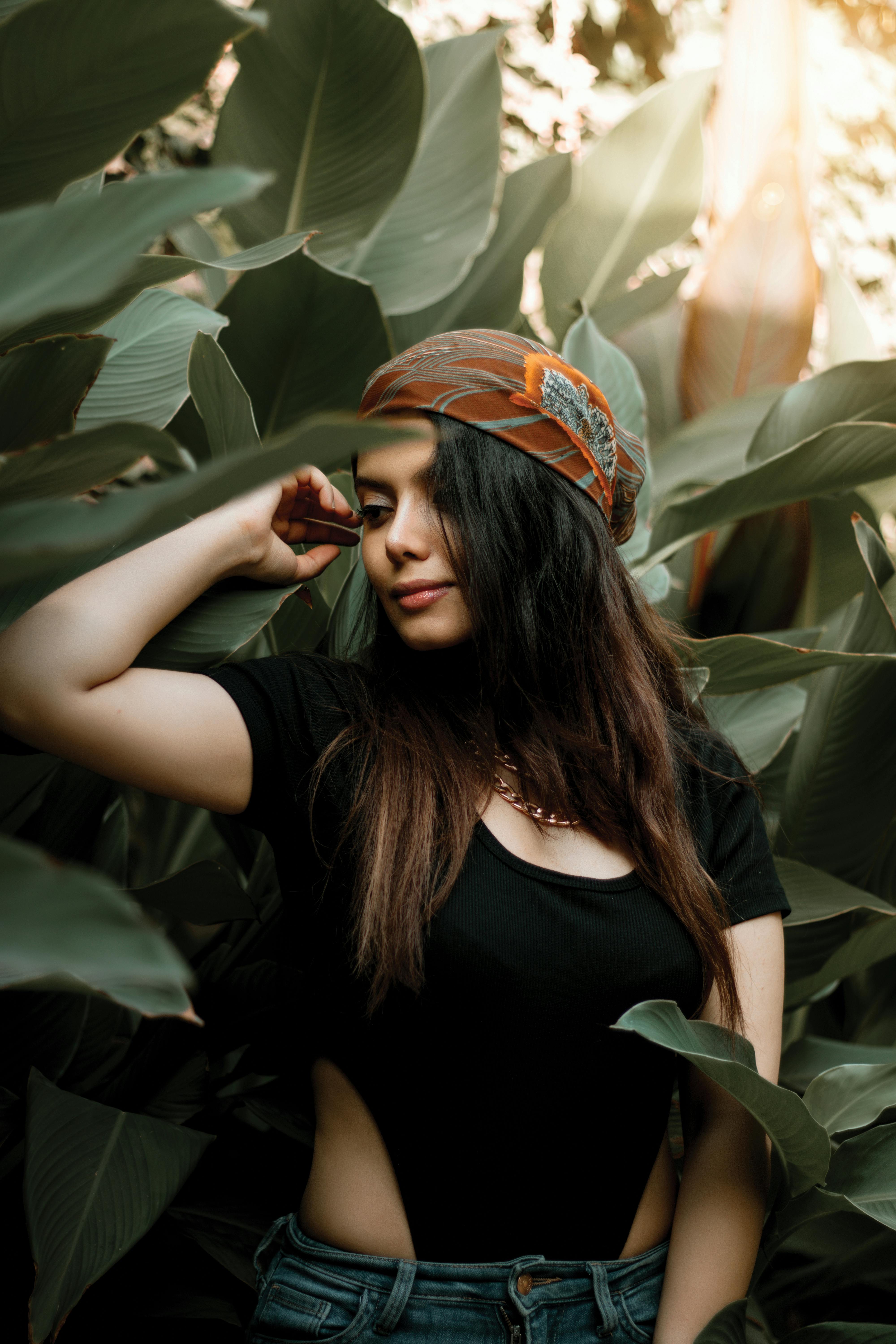Young woman with a headscarf posing among vivid green leaves, enjoying nature.