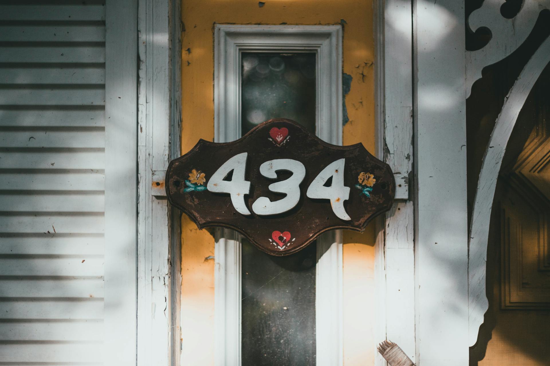 Close-up of an ornate vintage house number 434 sign with rustic wood design and charming hearts.