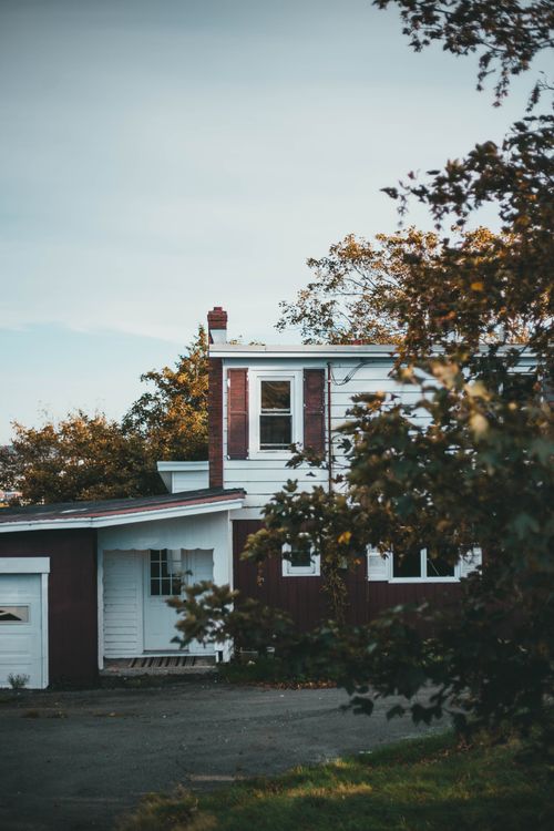 Free A quaint red and white house surrounded by lush trees under a clear sky, showcasing rustic charm. Stock Photo