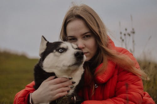 Free Woman in Red Jacket Hugging a Siberian Husky Stock Photo