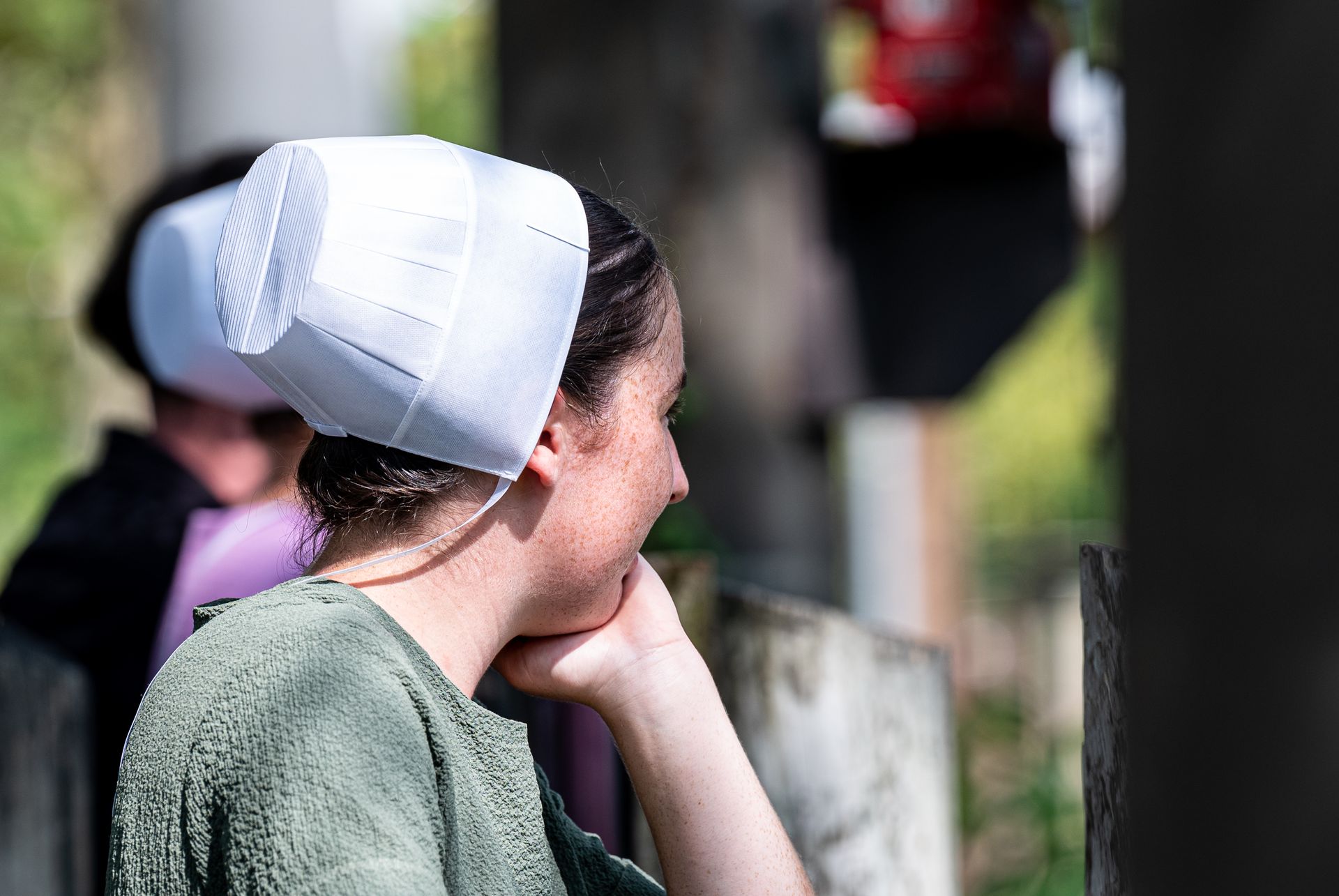 Side view of an Amish woman deep in thought, wearing a traditional prayer cap outdoors.