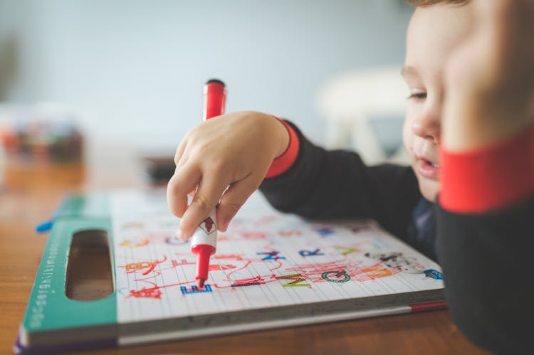 Boy Holding Marker Pen Writing On A Workbook