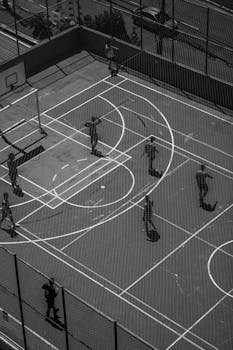 Monochrome aerial shot of people playing basketball on an outdoor court.