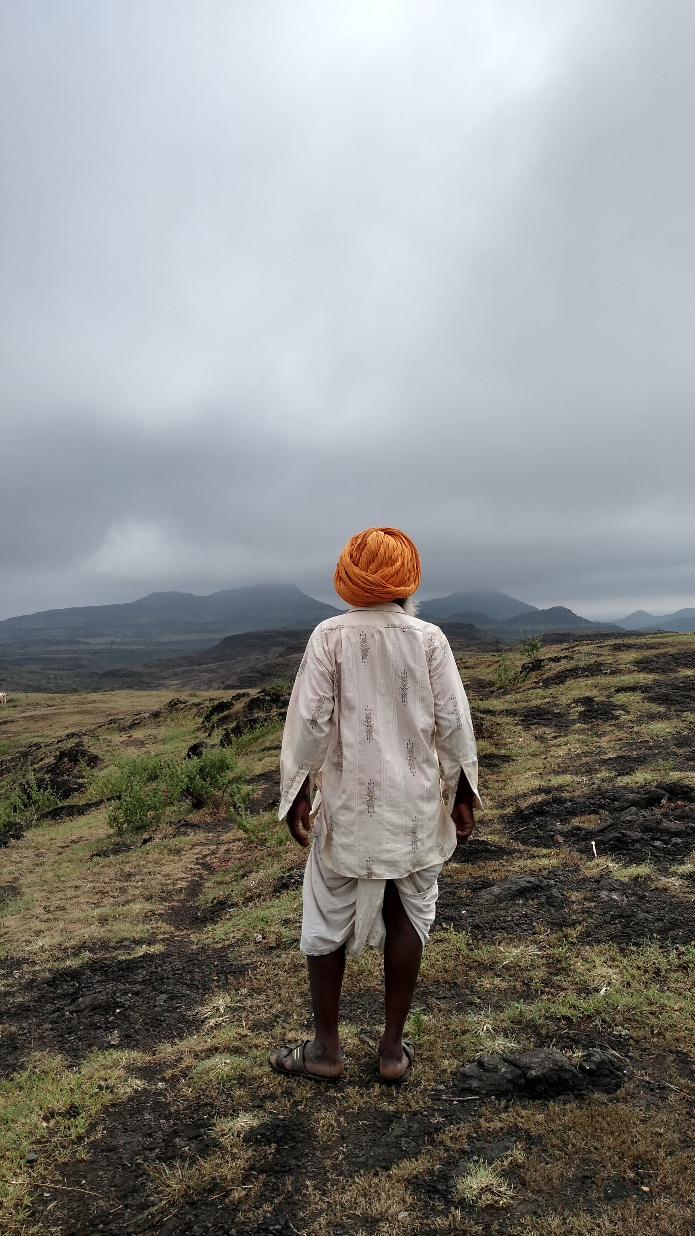 A solitary Indian man in traditional attire with a turban gazes over a misty, mountainous landscape.