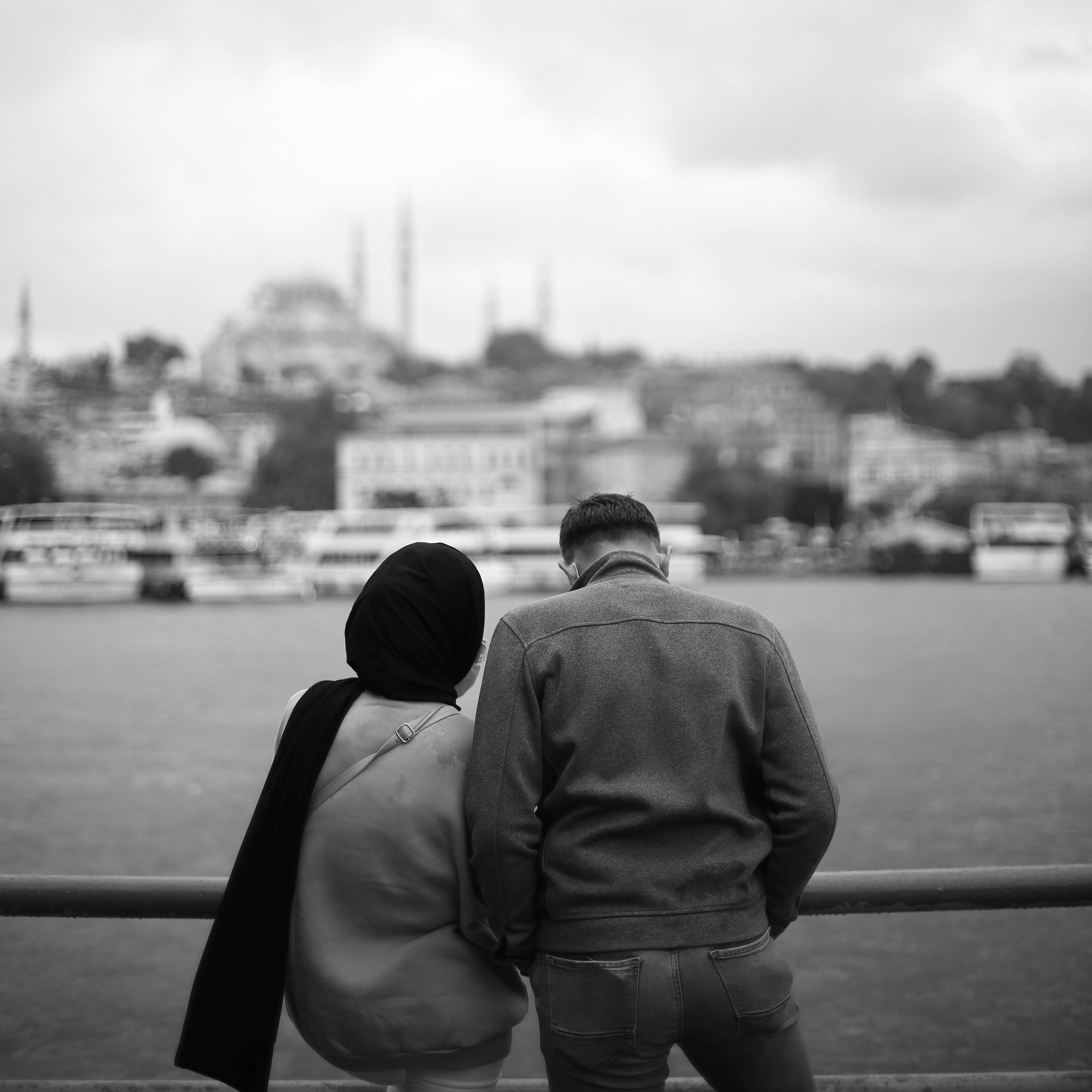 Black and white photo of a couple by the water with a cityscape of Istanbul in the background.