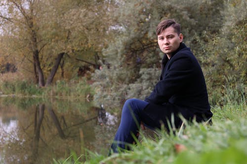 Free Man Wearing a Coat Sitting on the River Bank Stock Photo