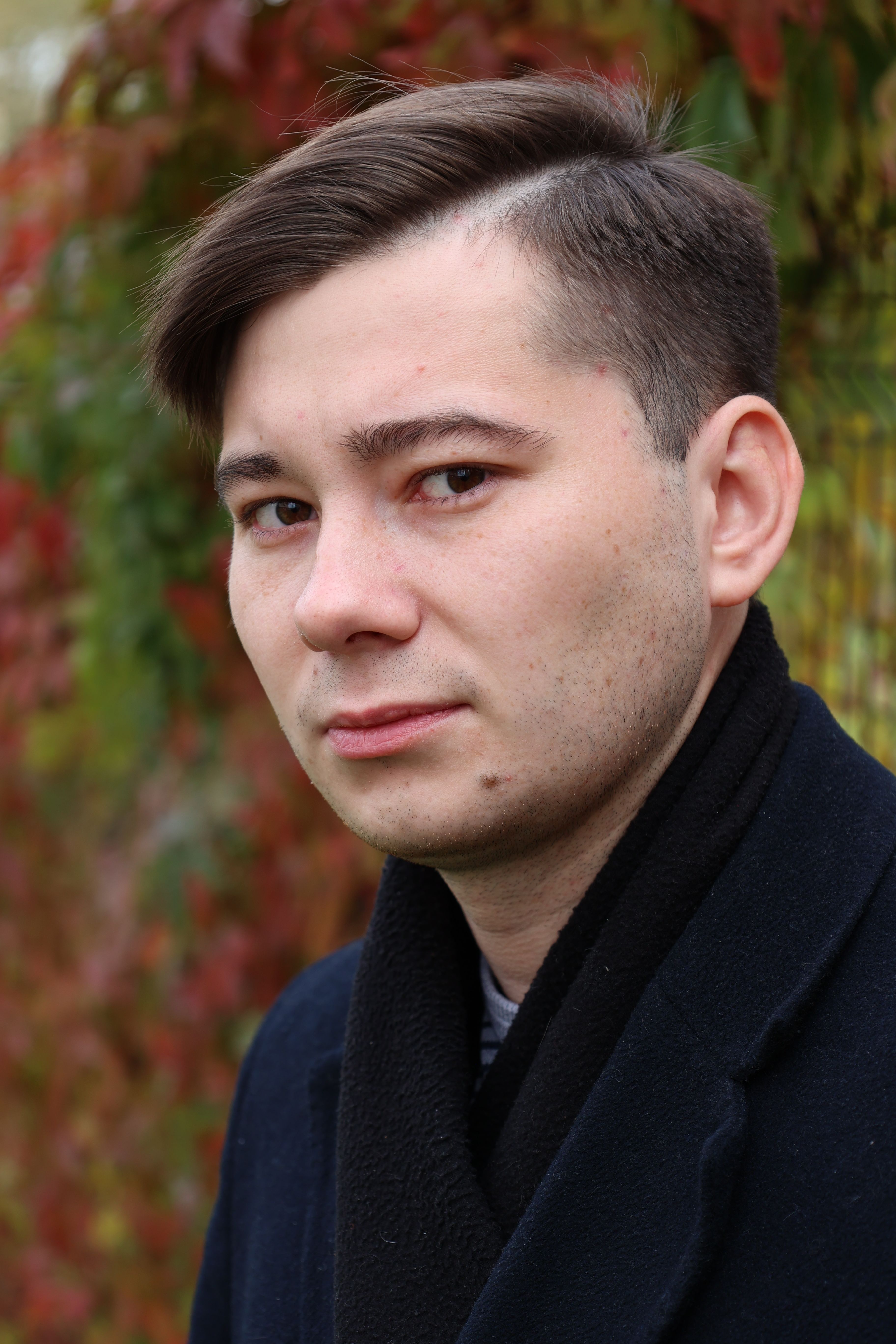 Close-up portrait of a young man outdoors with colorful autumn leaves in the background.