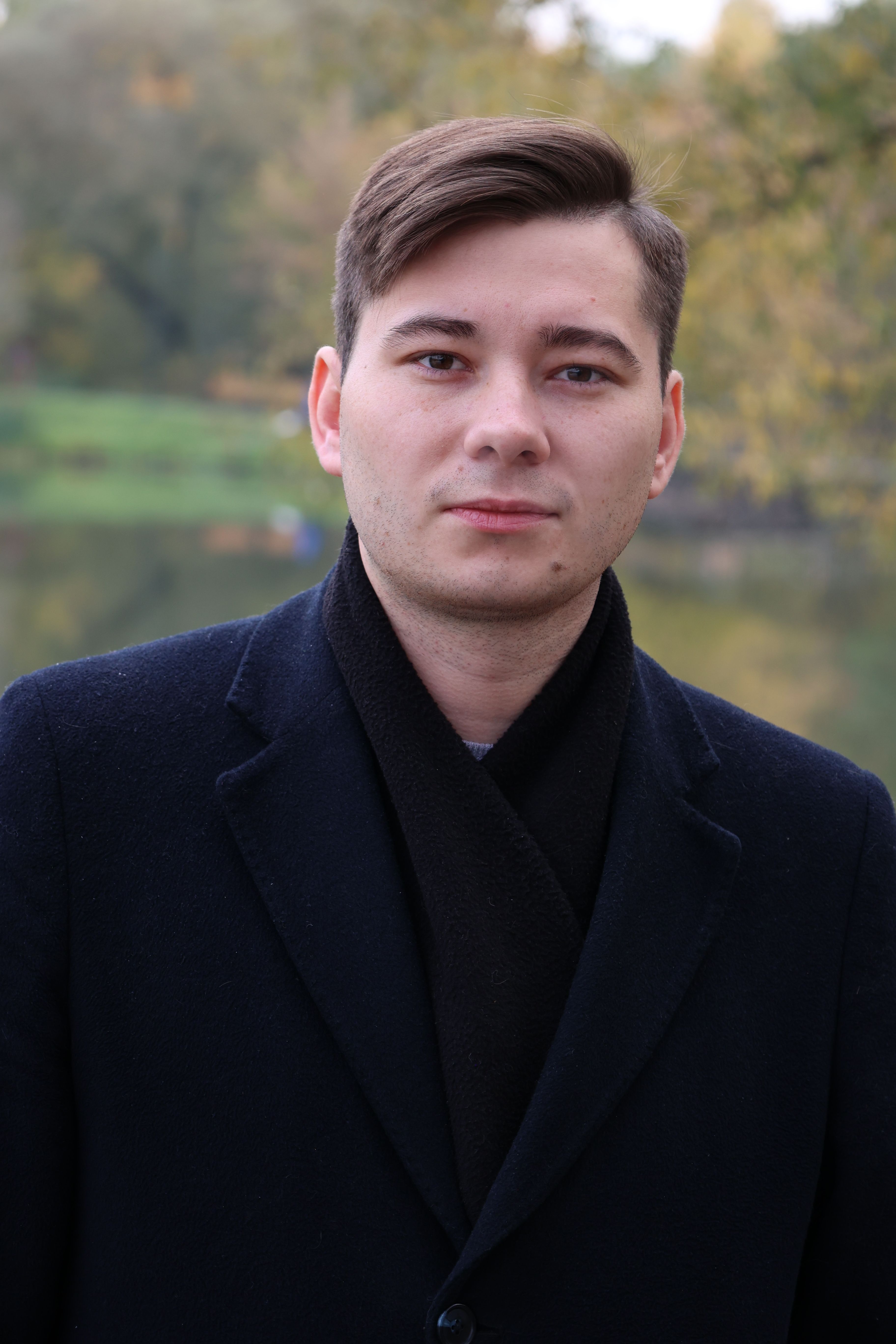 Close-up portrait of a man in a black coat outdoors during fall.