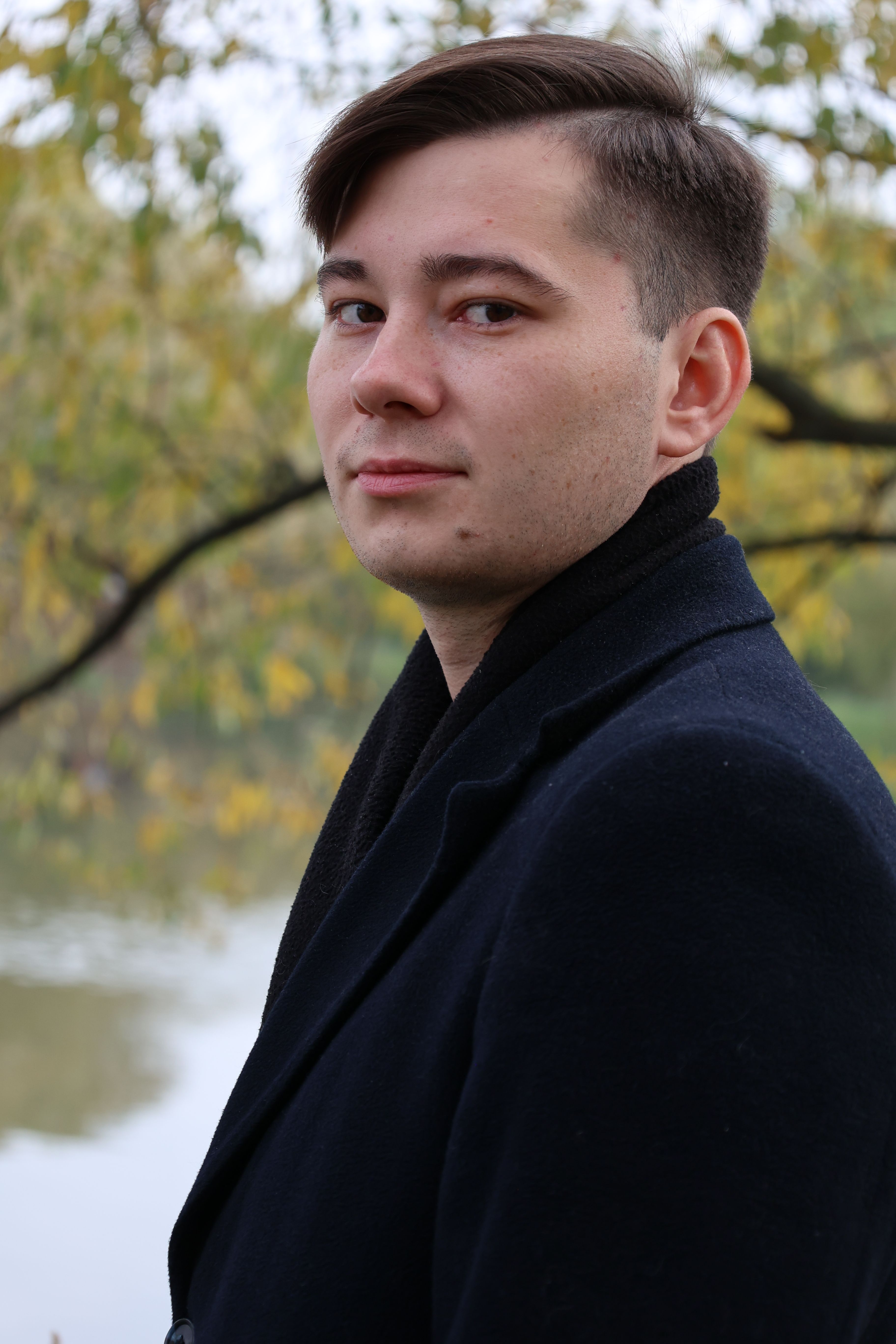 Side profile of a man in a black coat with autumn background.