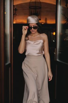Fashionable woman in satin blouse and hat stepping through doorway.
