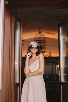 Chic woman wearing sunglasses and silk dress posing indoors with elegant decor.