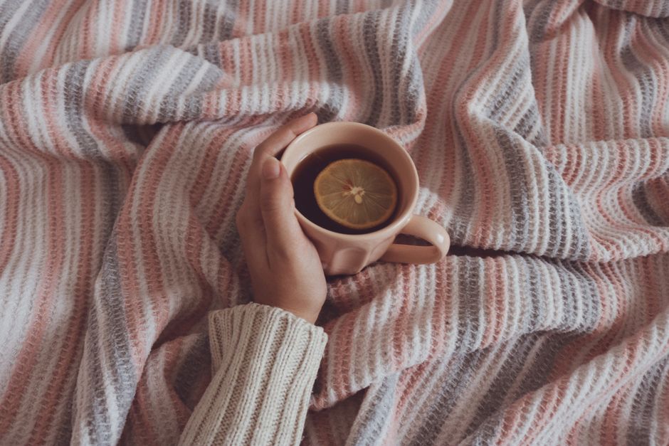 Warm cup of tea with a lemon slice held in hand on a comfy striped blanket.