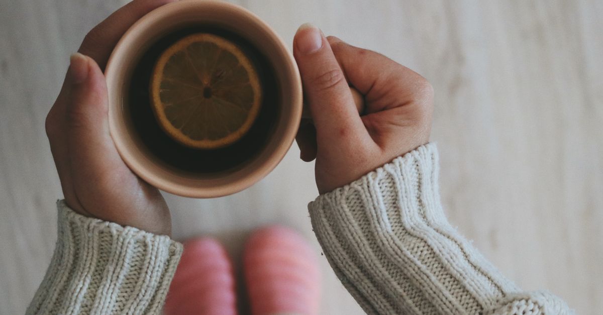 A warm cup of lemon tea held in cozy hands on a winter morning.
