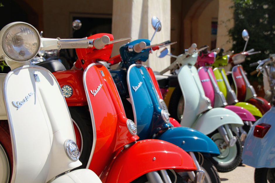 Vibrant Vespa scooters parked in the sunlit streets of Porto Cervo, Sardinia, Italy.