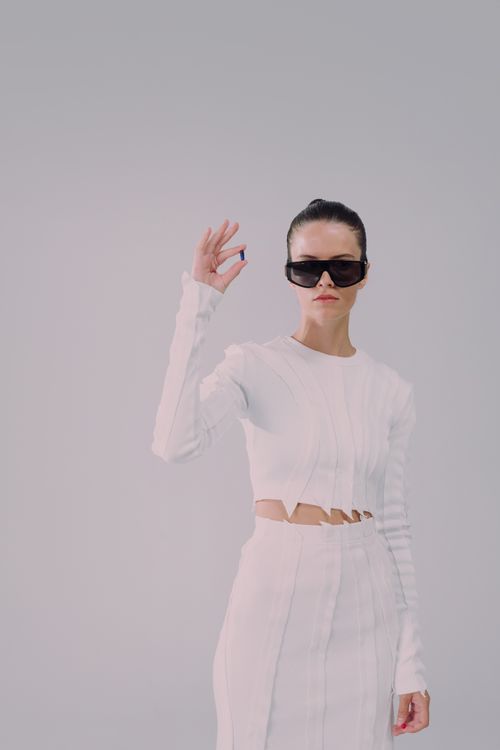 Free Chic woman in white attire holding a pill, wearing sunglasses, against a plain background. Stock Photo