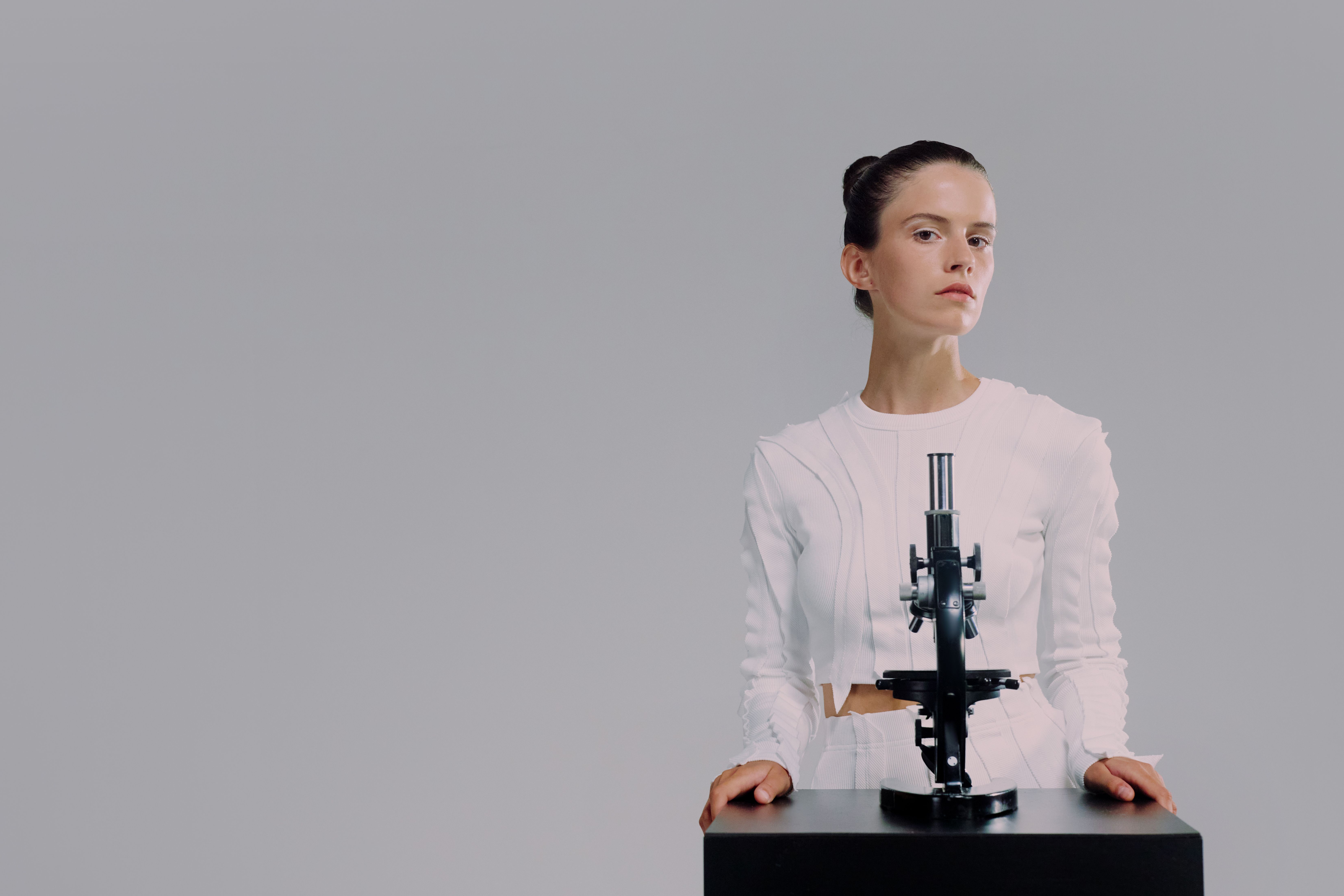 Scientist standing with microscope against a plain background in a studio setting.