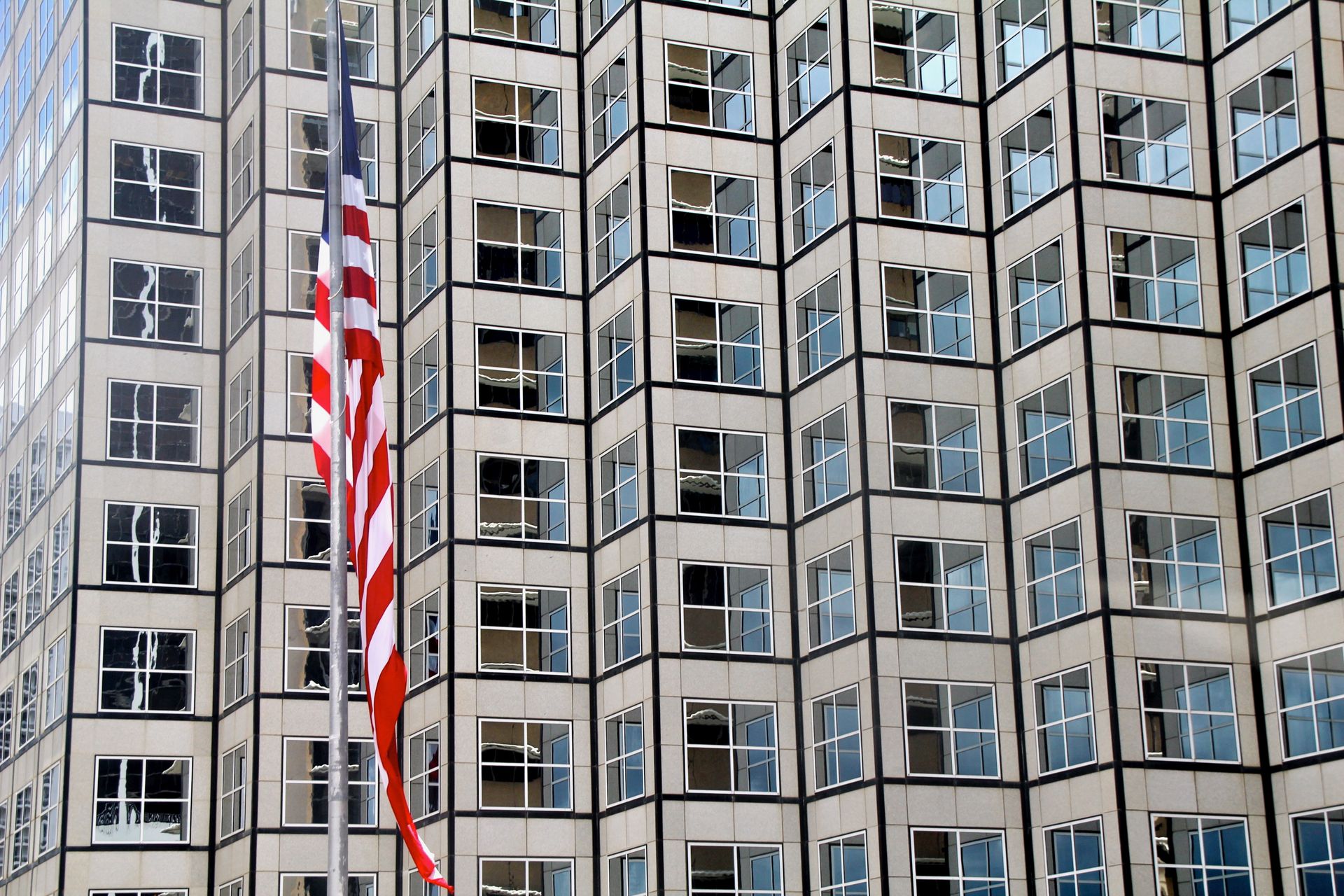 Geometric facade of a Miami building with American flag in foreground, sunny day.