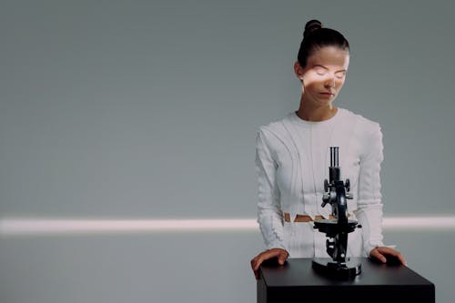 A female scientist standing behind a microscope and with a light falling on her eyes 