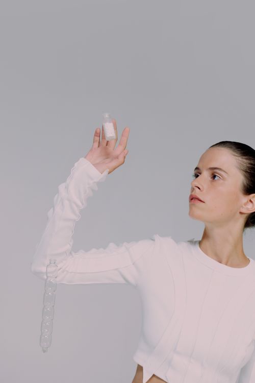Free Portrait of a female scientist in white holding a pill vial, set against a gray studio background. Stock Photo