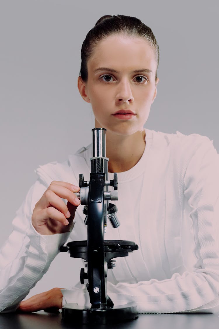 A Female Scientist Looking At Camera And Holding A Microscope