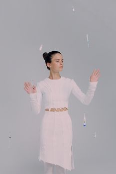 A woman in a white dress interacts with floating medical tools in a studio setting.