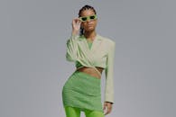 穿着绿色服装、戴着灰色背景太阳镜的时尚年轻女子