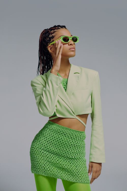 Free Chic and stylish woman in green outfit and sunglasses posing confidently in a studio. Stock Photo