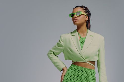 Free Chic woman in green blazer and skirt with sunglasses, posing confidently. Stock Photo