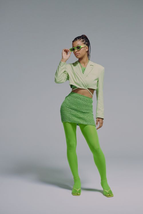 Free Stylish adult woman in a green ensemble with sunglasses, posing in a studio. Stock Photo