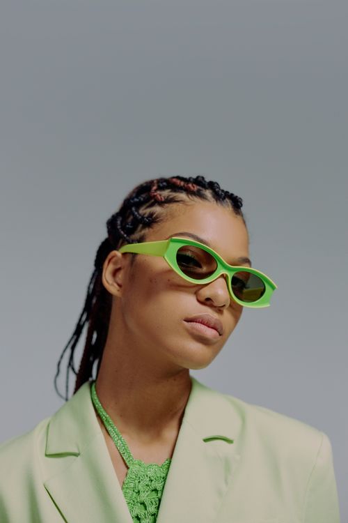 Free Stylish portrait of a woman wearing green sunglasses and blazer in studio setting. Stock Photo