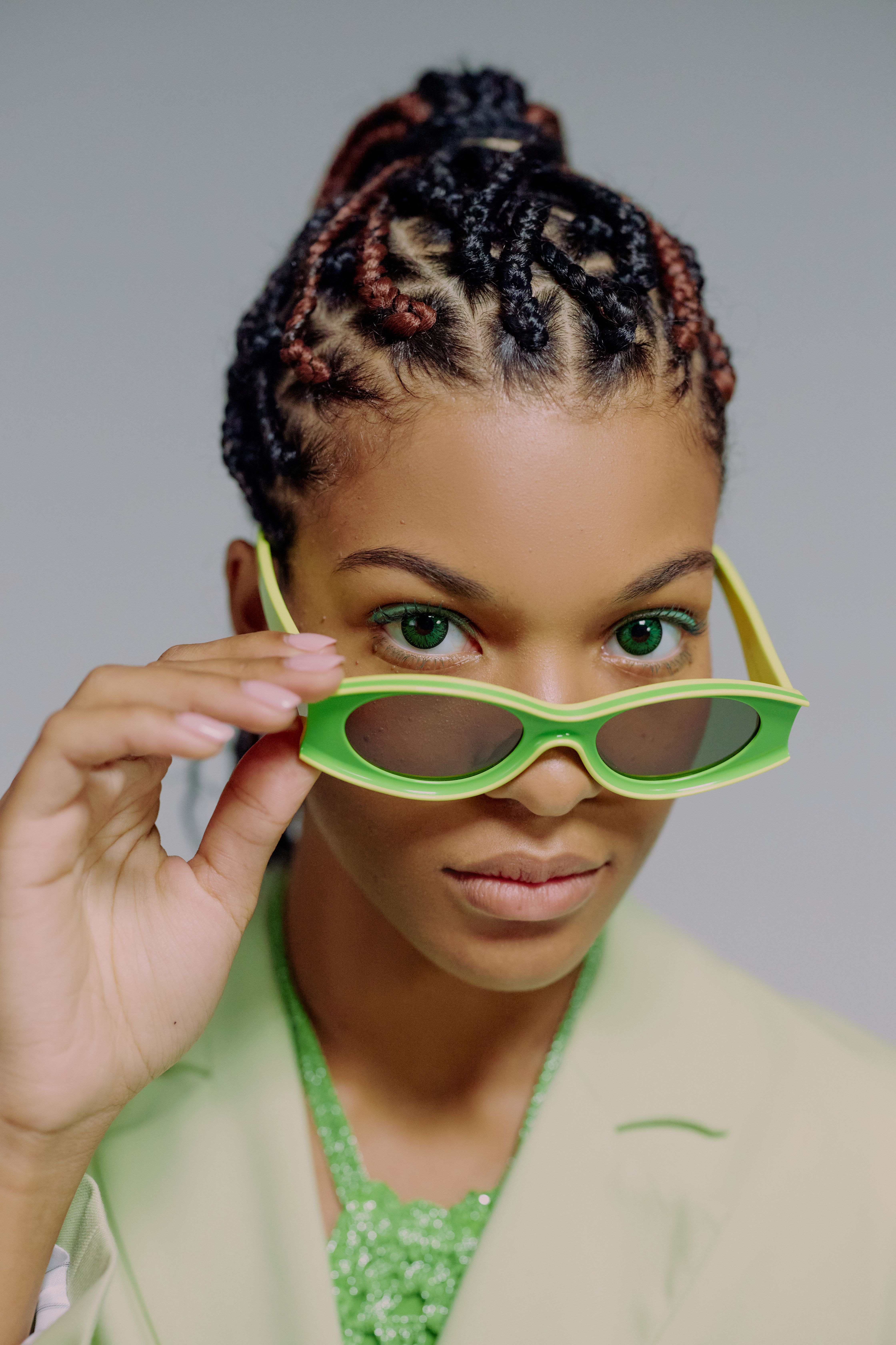 Portrait of a fashionable woman in green sunglasses and elegant attire, looking confidently at the camera.