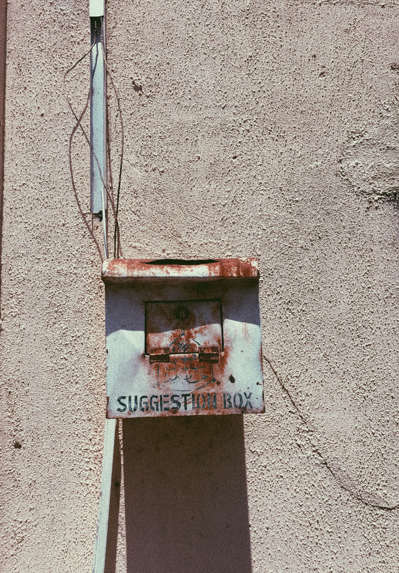 A rusted suggestion box mounted on a weathered wall