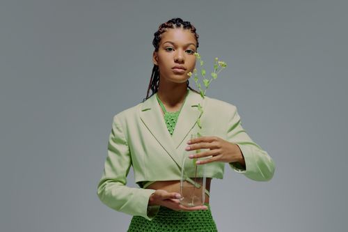 Free Stylish woman in green suit holding a glass vase with plant against a neutral backdrop. Stock Photo