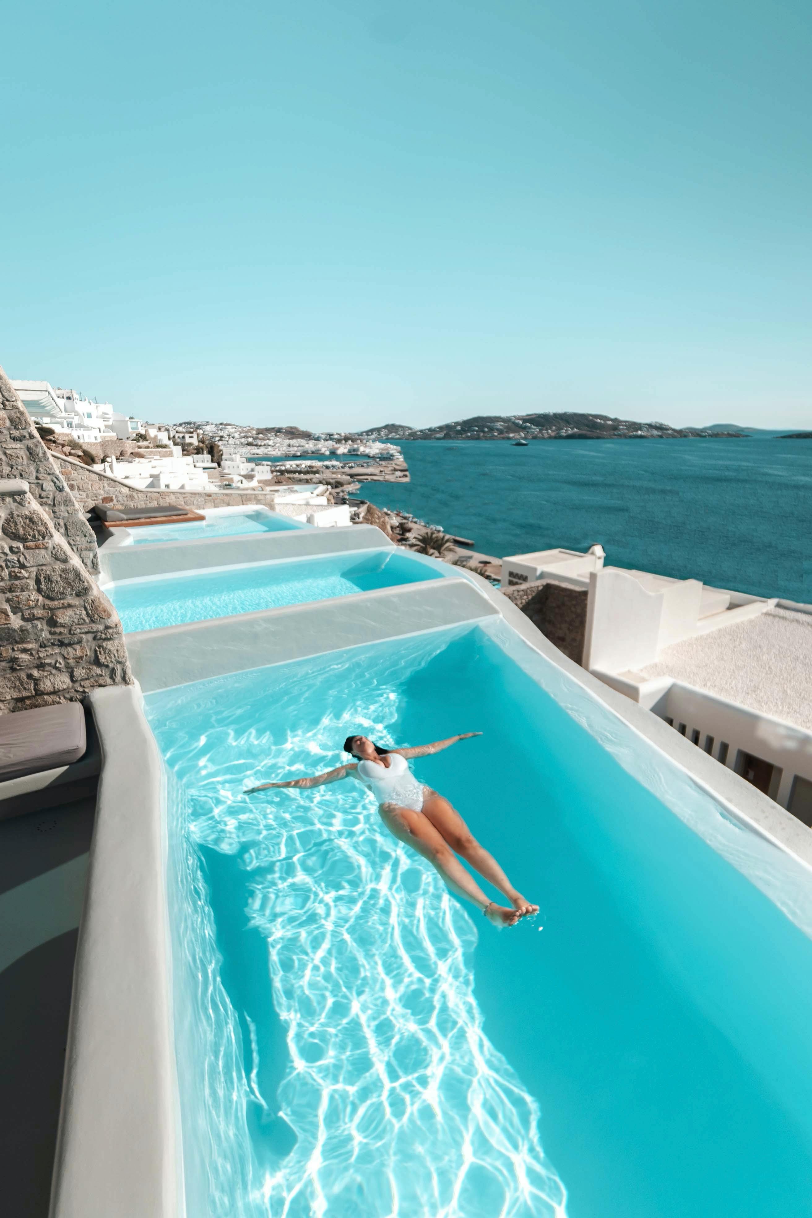 Woman enjoying a sunny day in a luxurious pool overlooking the ocean in Mykonos.