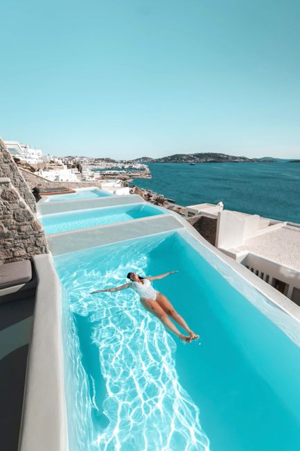 Woman enjoying a sunny day in a luxurious pool overlooking the ocean in Mykonos.