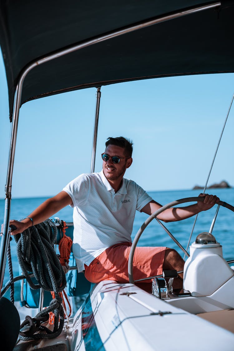 Stylish Man In White Polo Shirt Driving A Yacht 