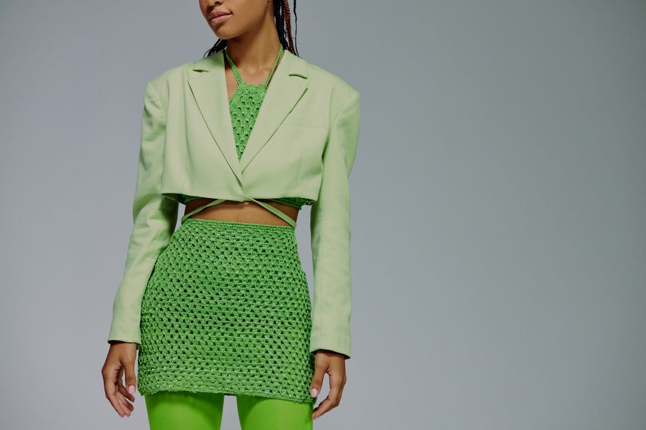 Chic woman in a green ensemble posing against a plain studio backdrop.